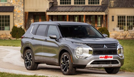 Un todoterreno Mitsubishi plateado estacionado frente a una casa moderna con grandes ventanas y detalles de piedra.